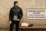 A stylish young man in his mid-20s wearing a black leather jacket layered over a knit sweater, slim dark jeans, brown Chelsea boots, and a grey wool scarf, standing against a rustic urban background. Beside him on a wooden bench are folded winter essentials like a chunky sweater, leather gloves.